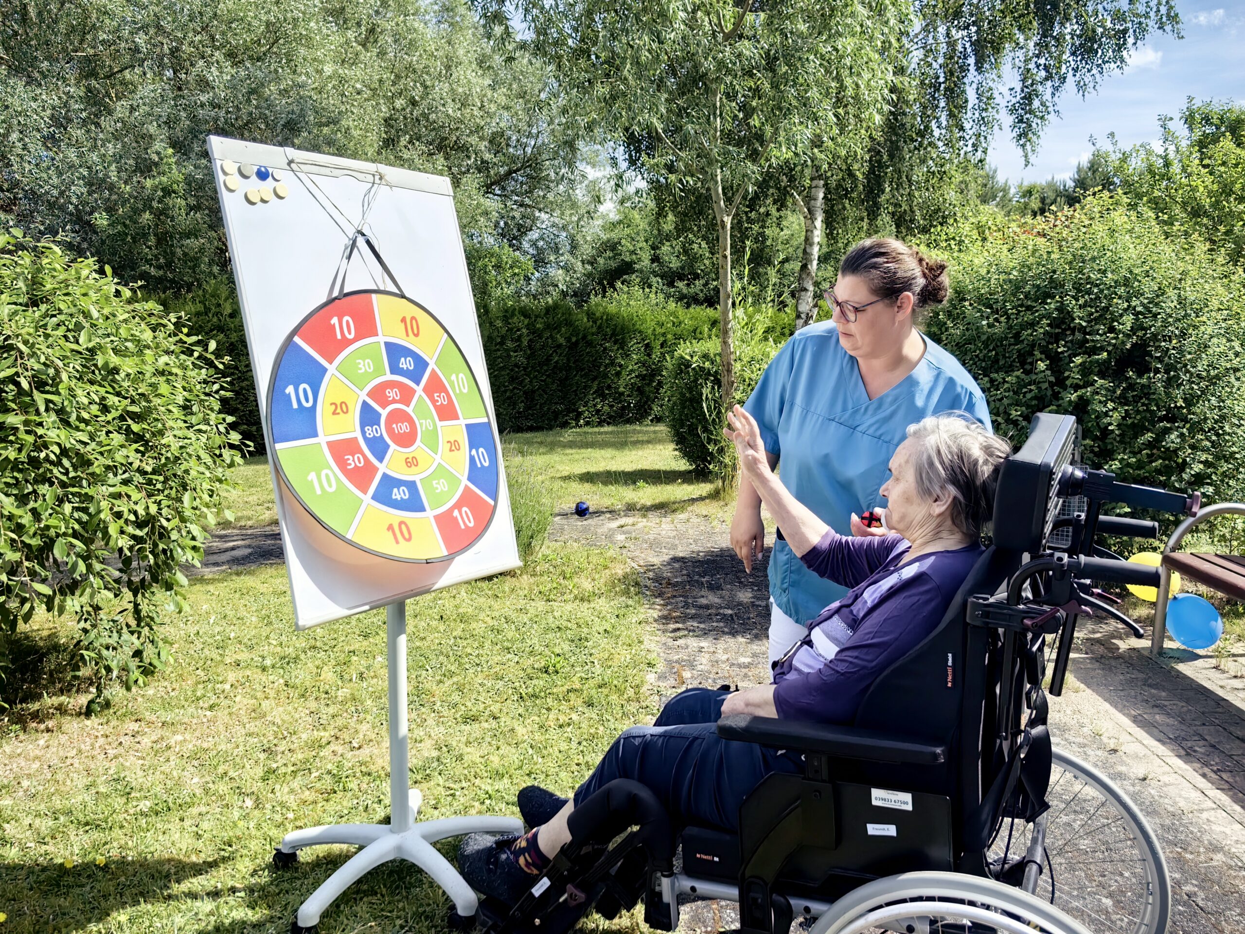Seniorin in Rollstuhl und Pflegerin beim Dartball spielen